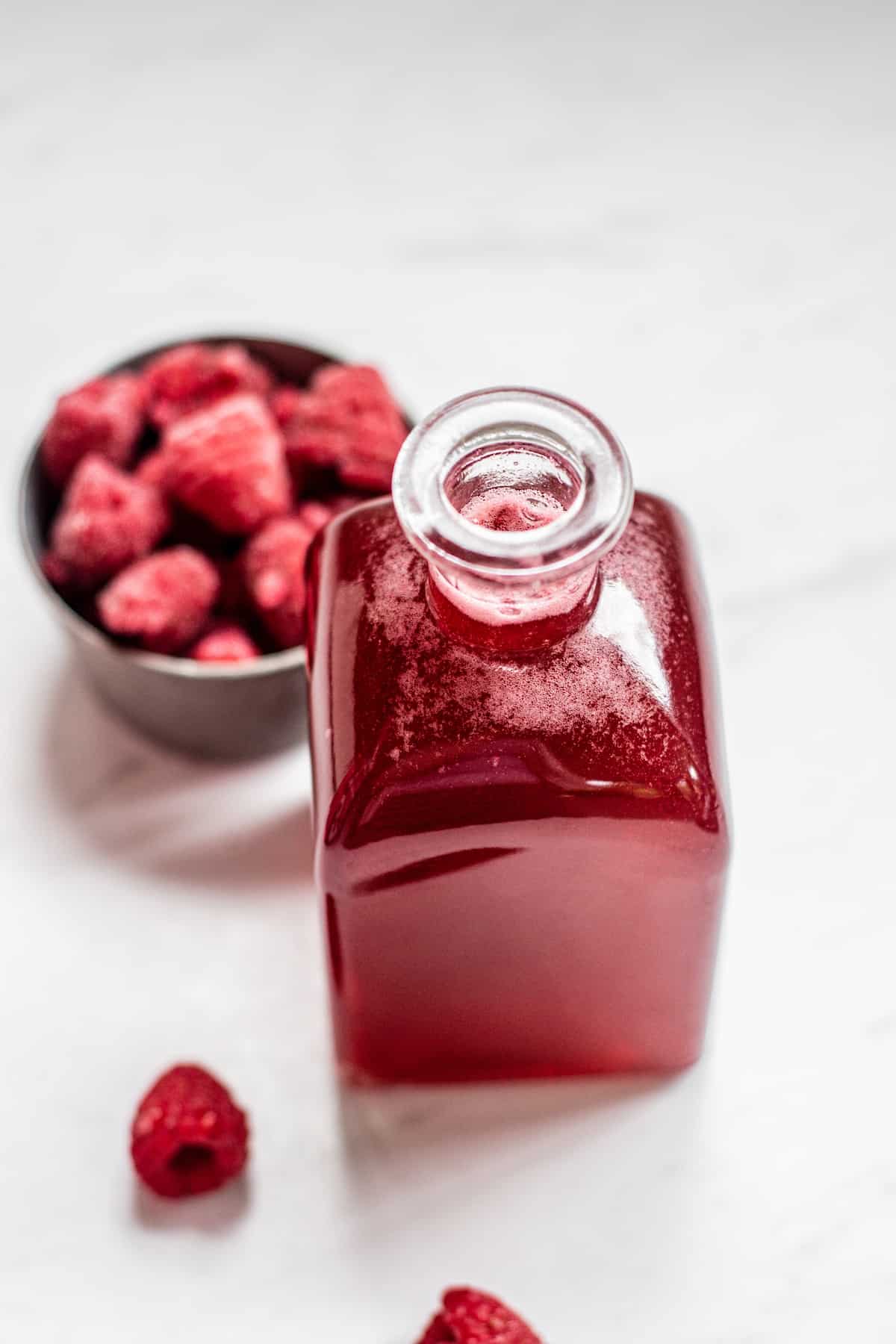 red syrup with raspberries in the background.