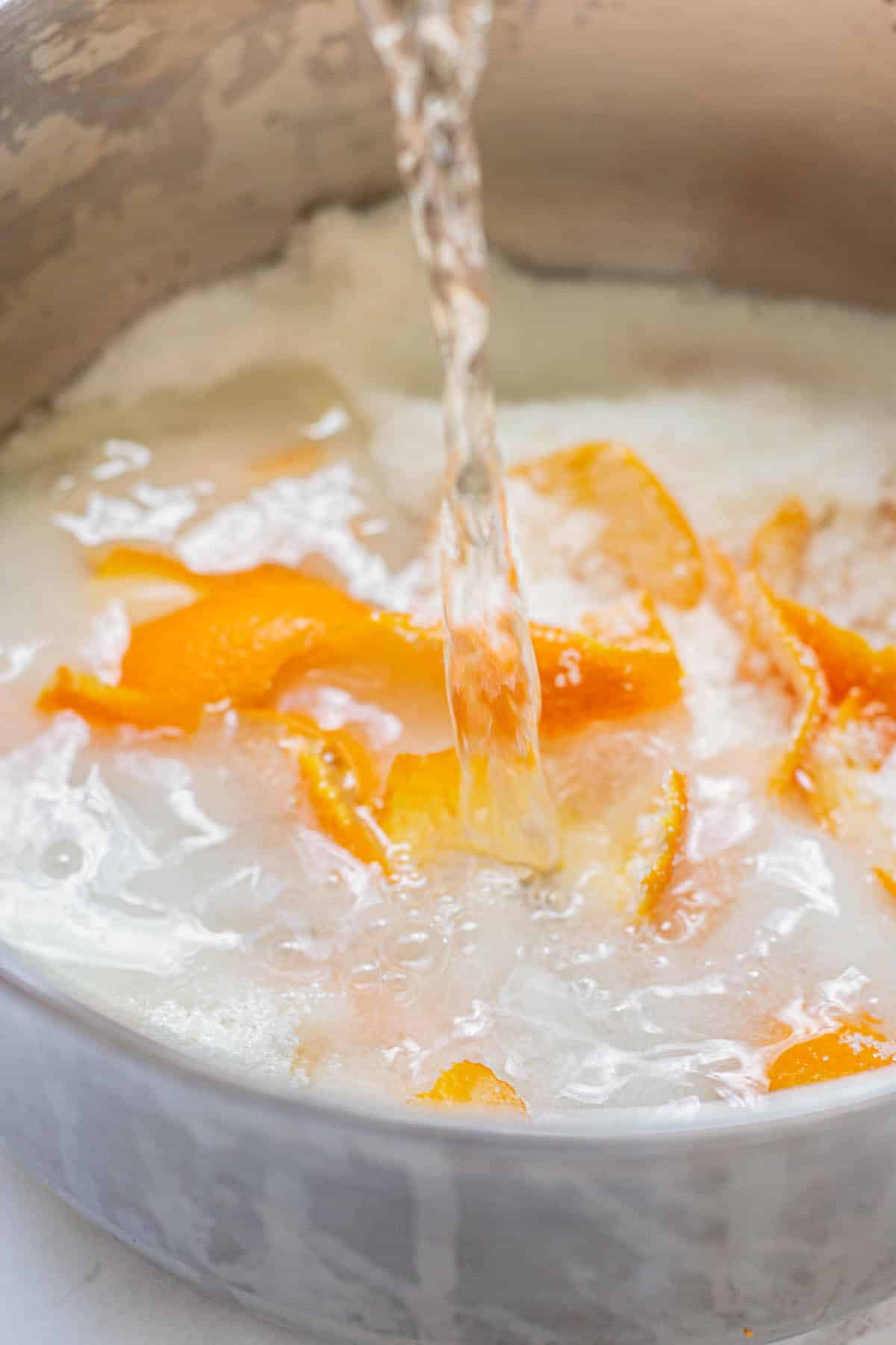 water being poured onto sugar and orange peel in a pot.