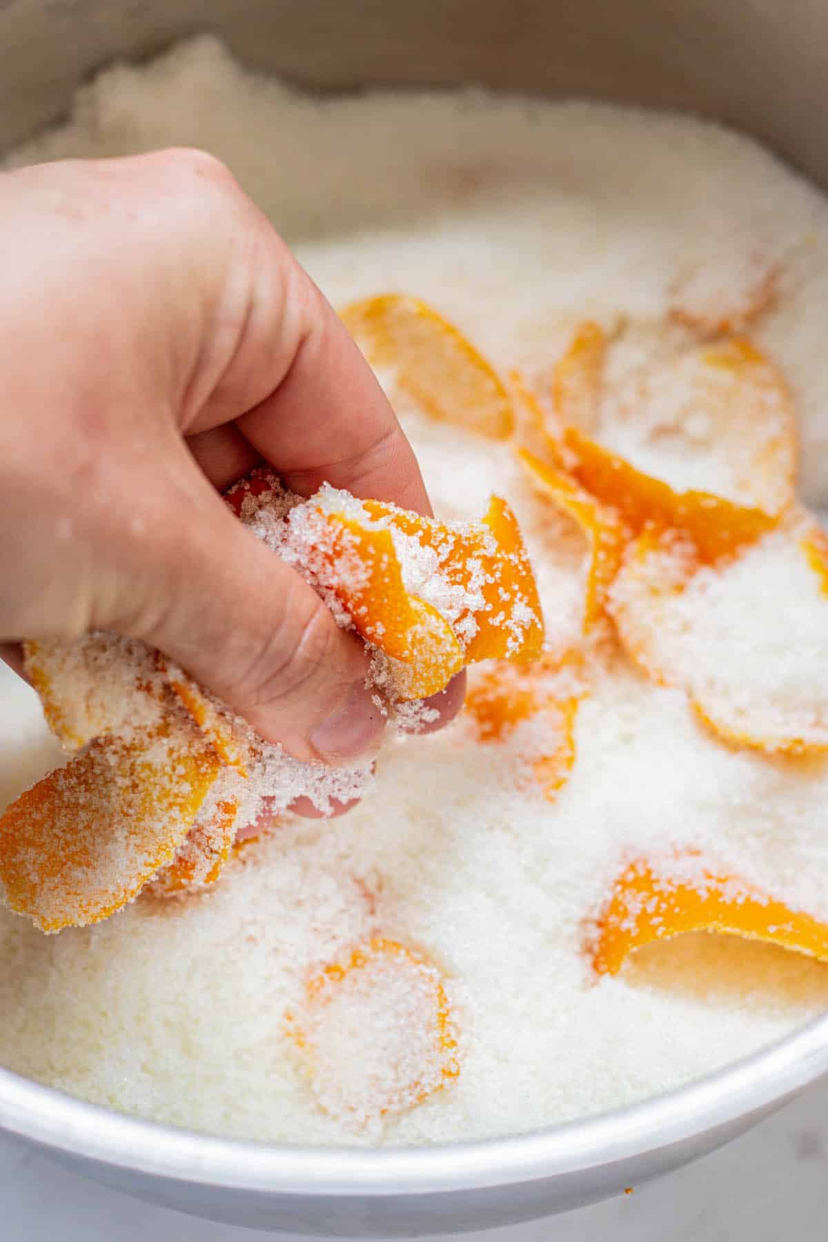 hand rubbing orange peels covered in sugar.