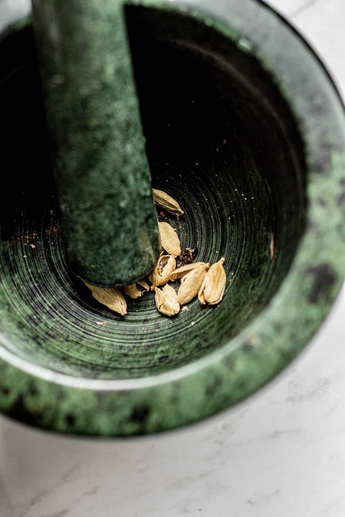 cardamom in a green mortar and pestle being crushed.