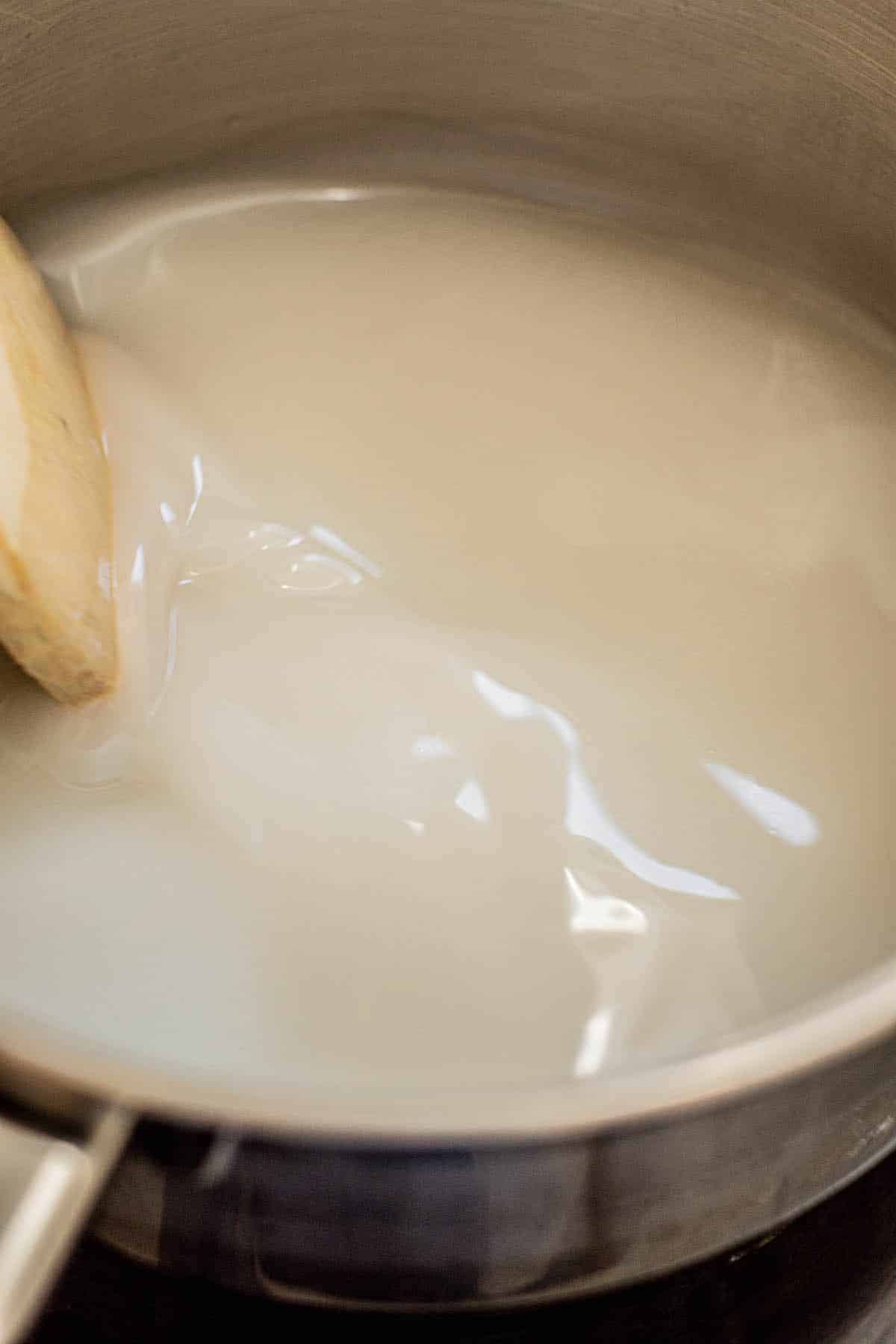 cream of coconut being stirred in a pot by wooden spoon.
