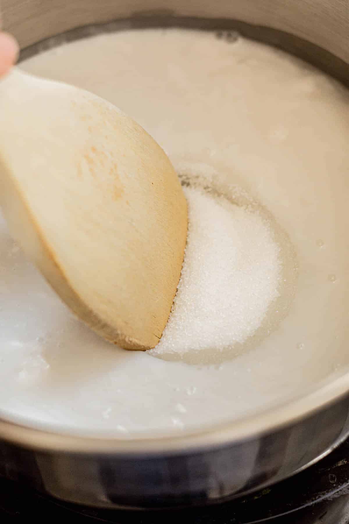 cream of coconut being made in a pot by wooden spoon with sugar not dissolved.