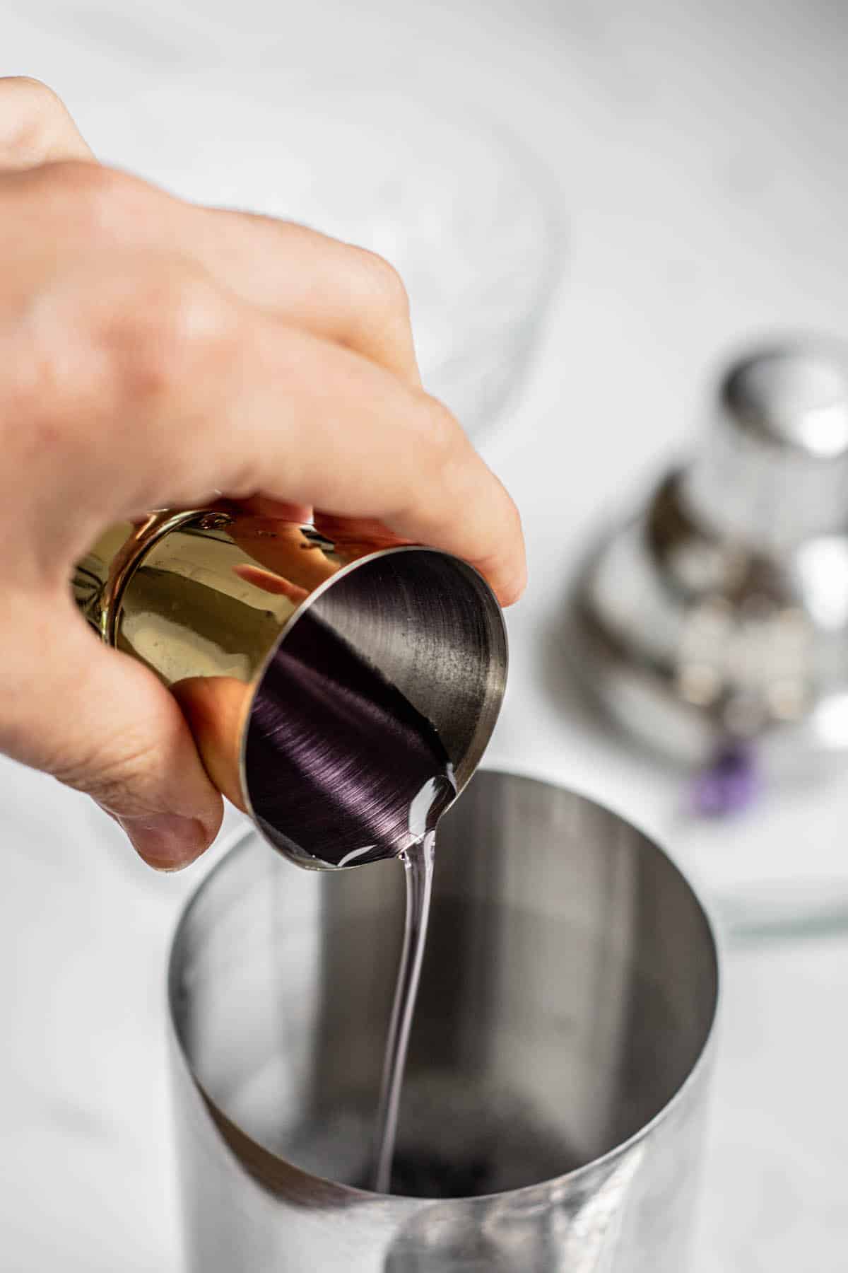 lavender syrup being poured into a cocktail shaker.