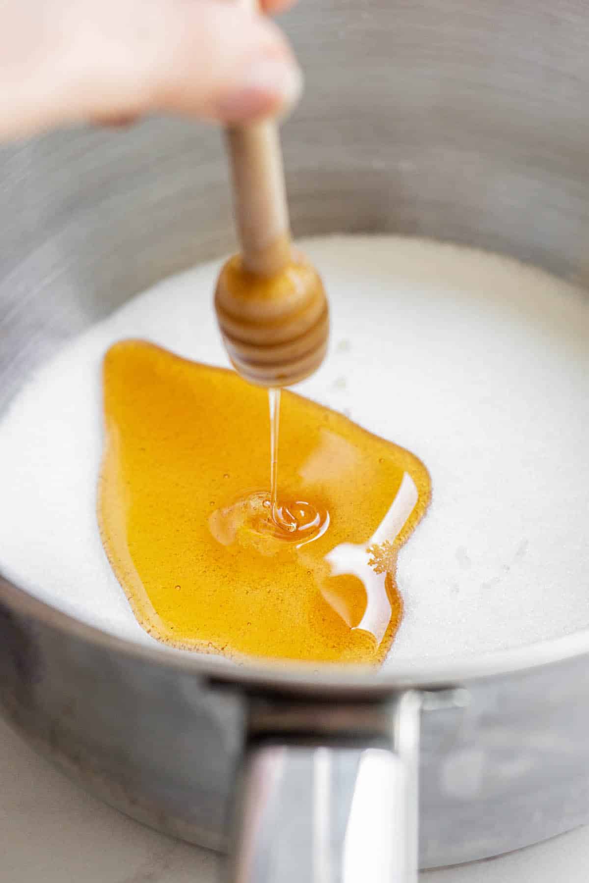 honey lavender syrup being made in a small saucepan with honey being drizzled over sugar.