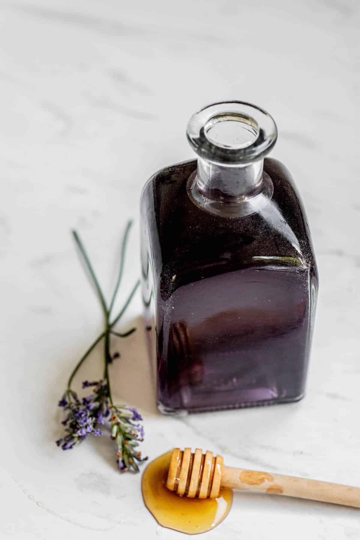 small glass bottle of honey lavender syrup with lavender and next to it.