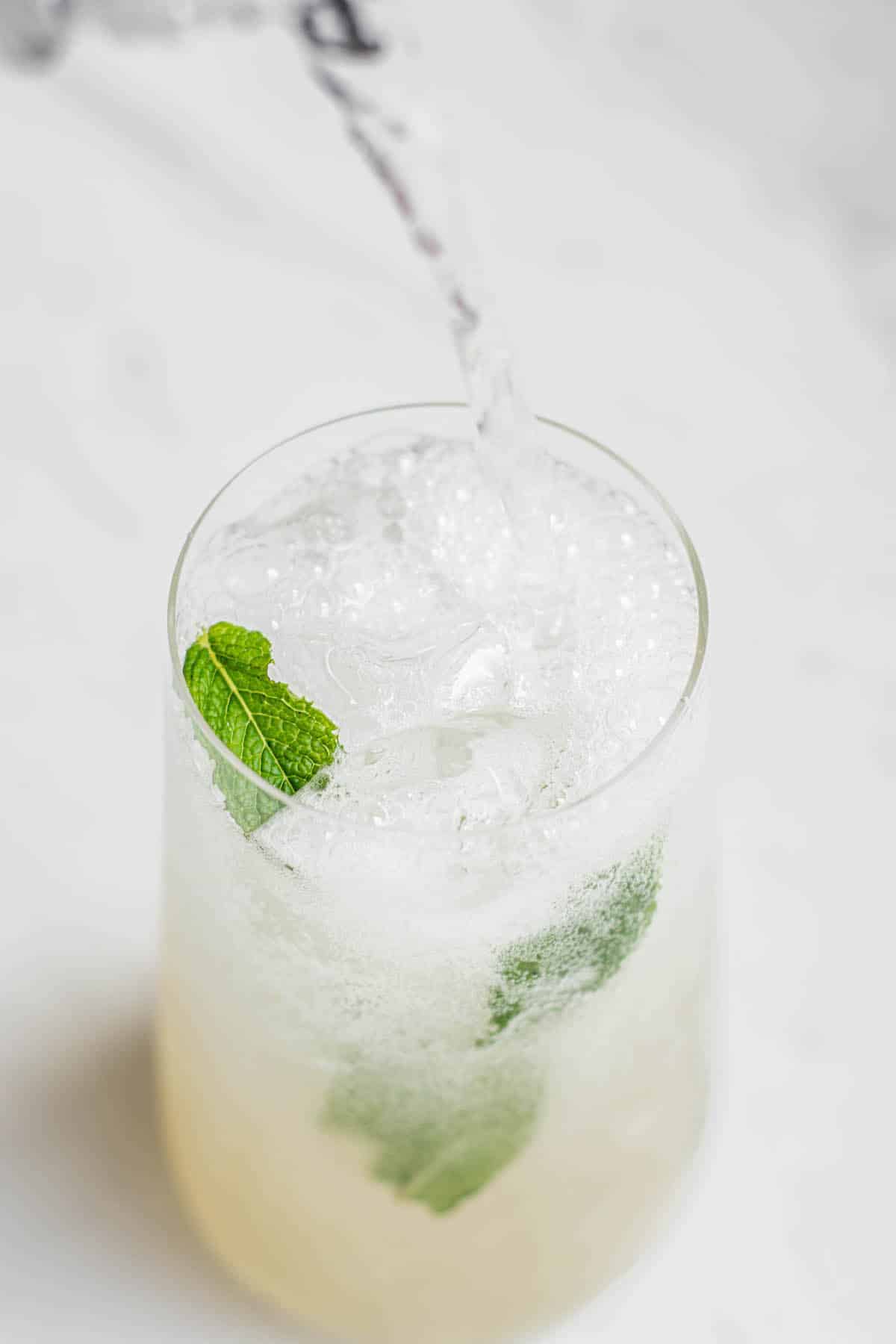 lychee mojito in a tall glass with mint being toped up with soda water.
