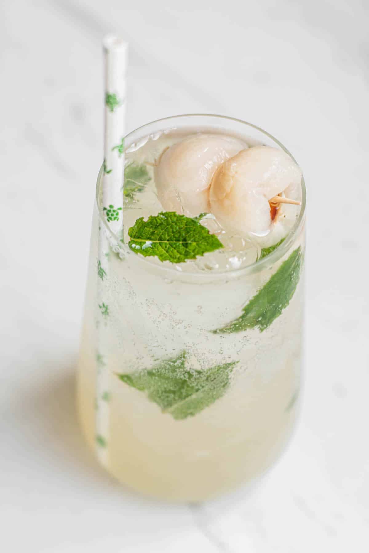lychee mojito in a tall glass with mint and straw with little green turtles on it.