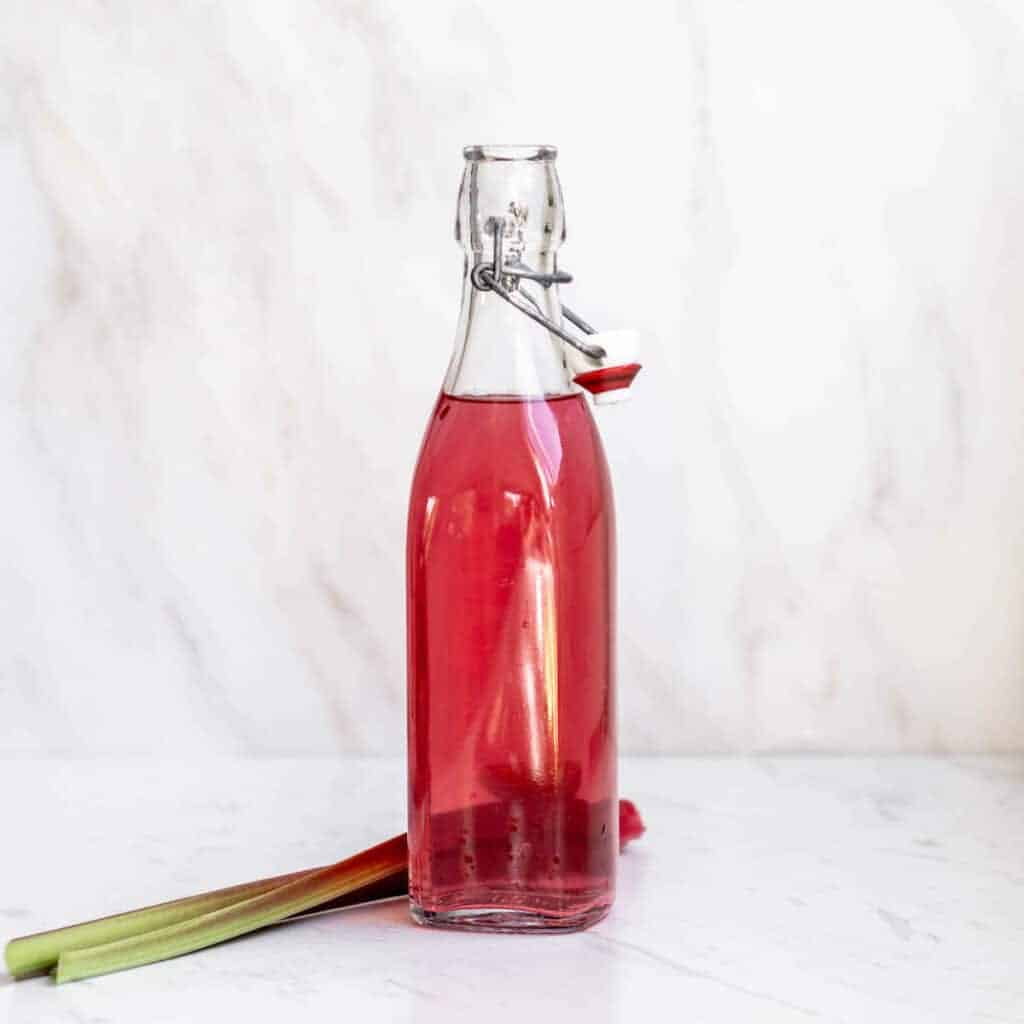 rhubarb infused vodka in a bottle with a rhubarb on the side next to the bottle.