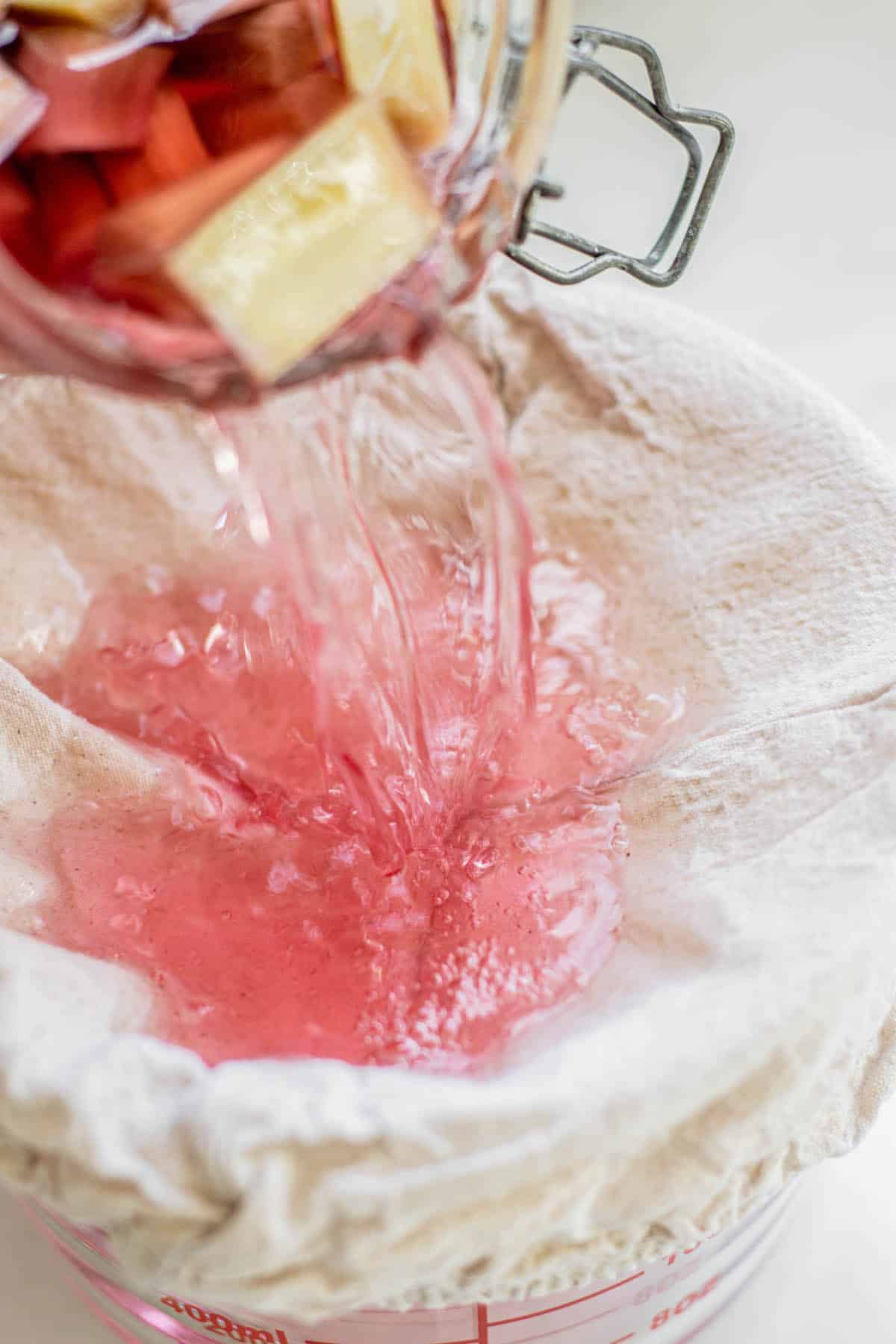 cooked rhubarb being poured into a muslin cloth into a glass bowl.
