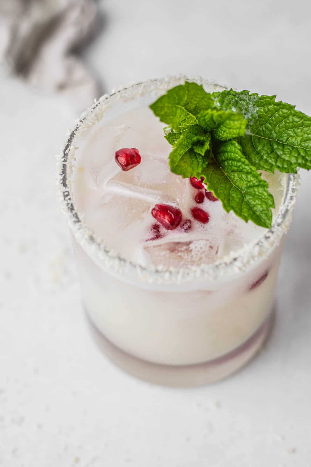 coconut rimmed glass filled with white drink, red pomegranate seeds and mint leaves.