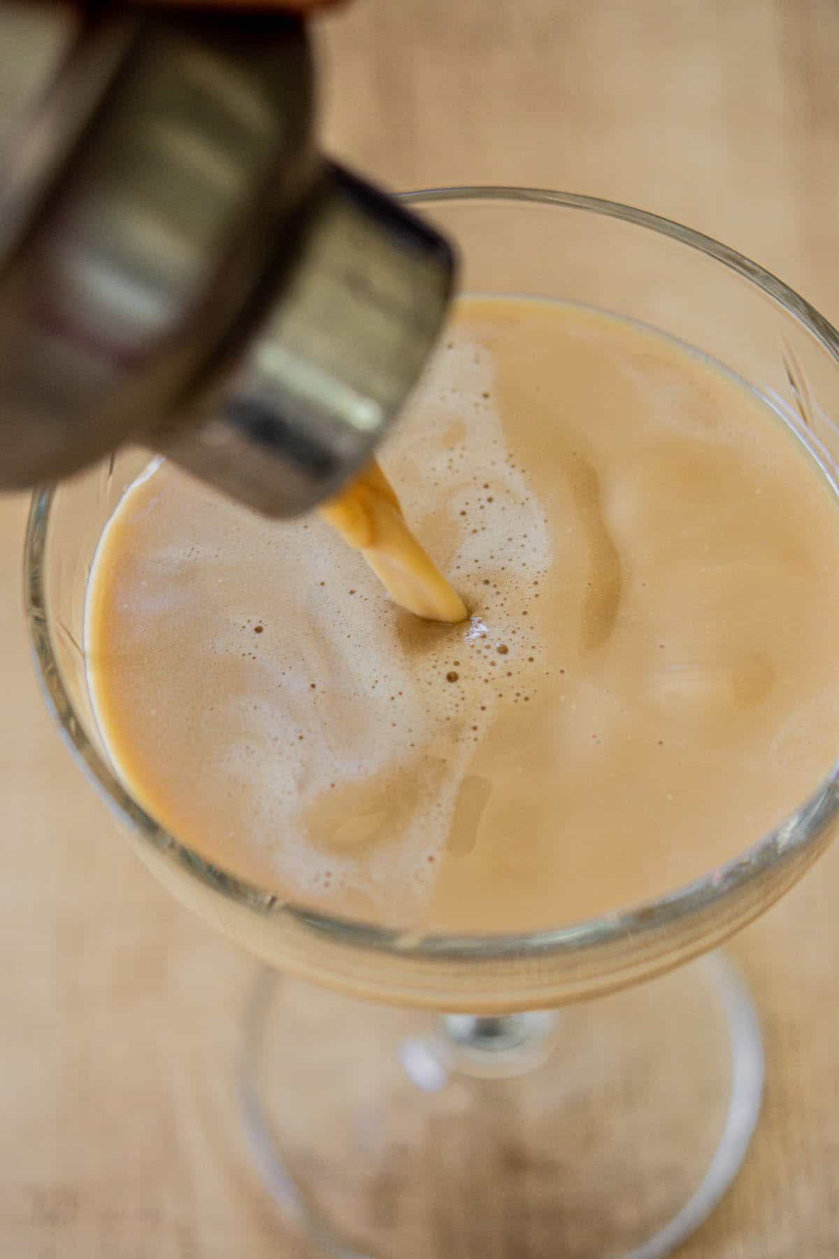 milky brown cocktail being poured.