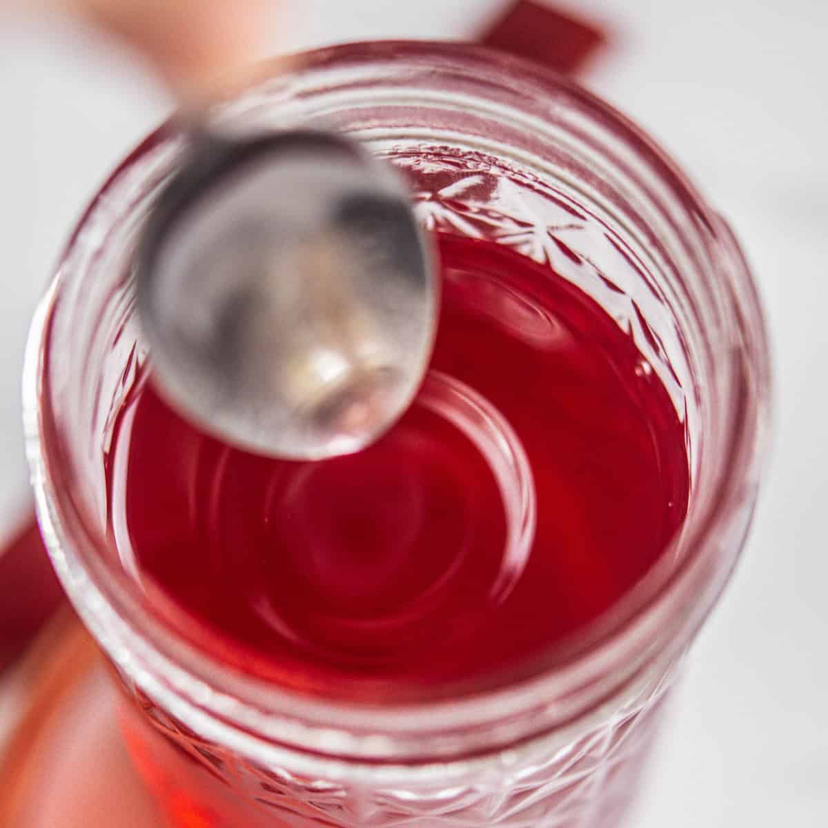 spoon dipping into red syrup.