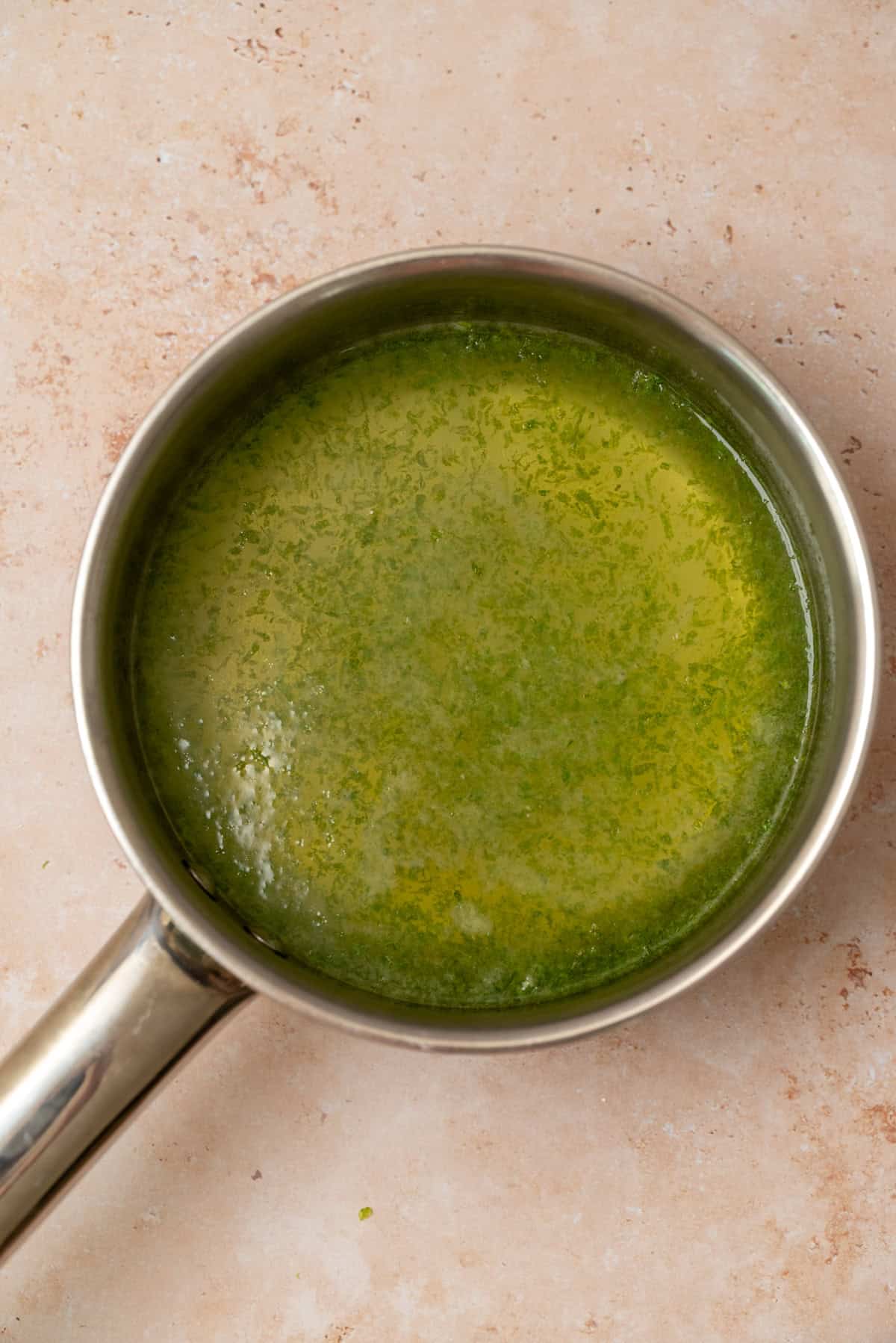 A stainless steel saucepan containing lime zest and water sitting on a light beige countertop.