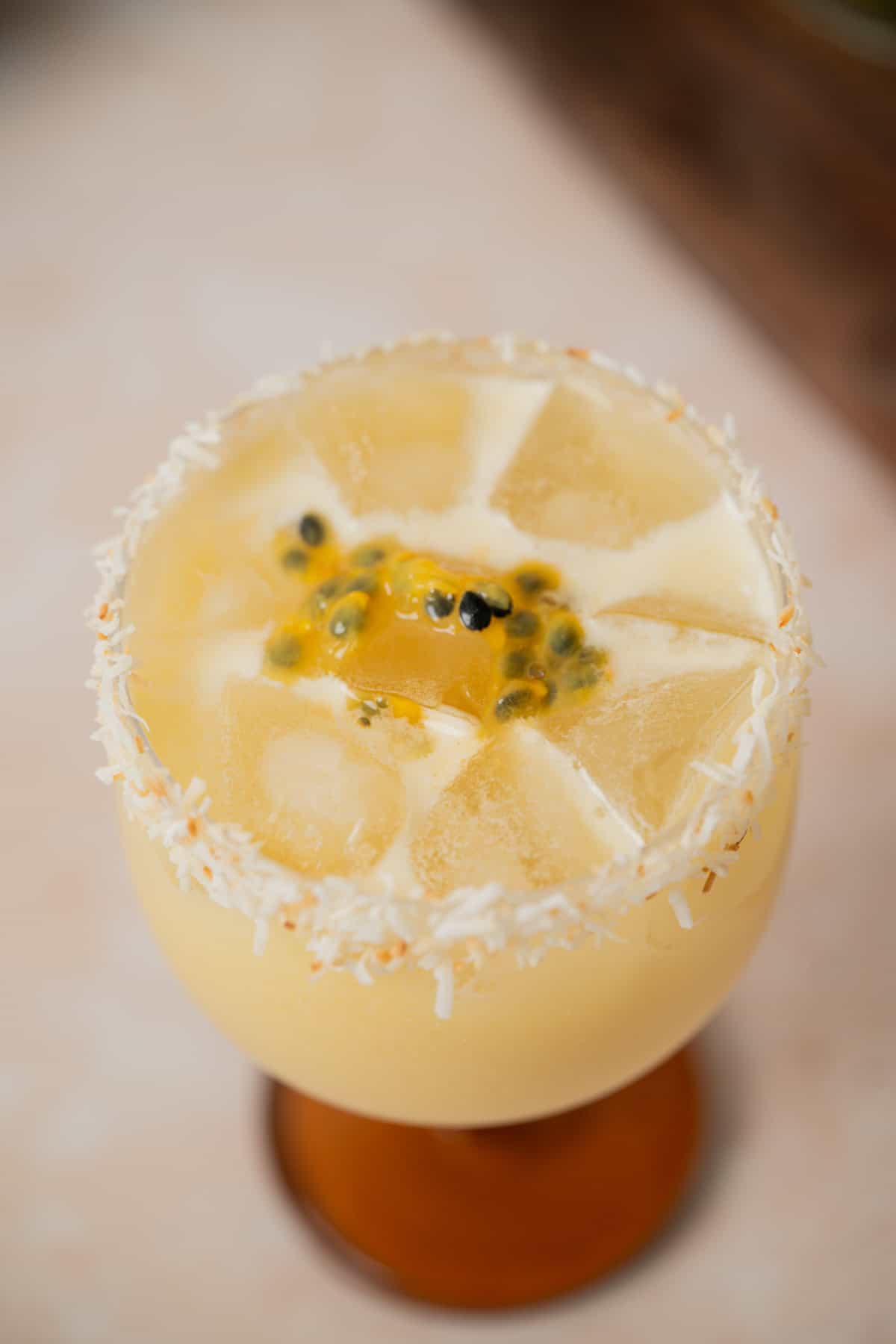 A creamy passionfruit coconut daiquiri with ice cubes, garnished with passion fruit pulp in the center and shredded coconut around the rim, served in a wide glass.
