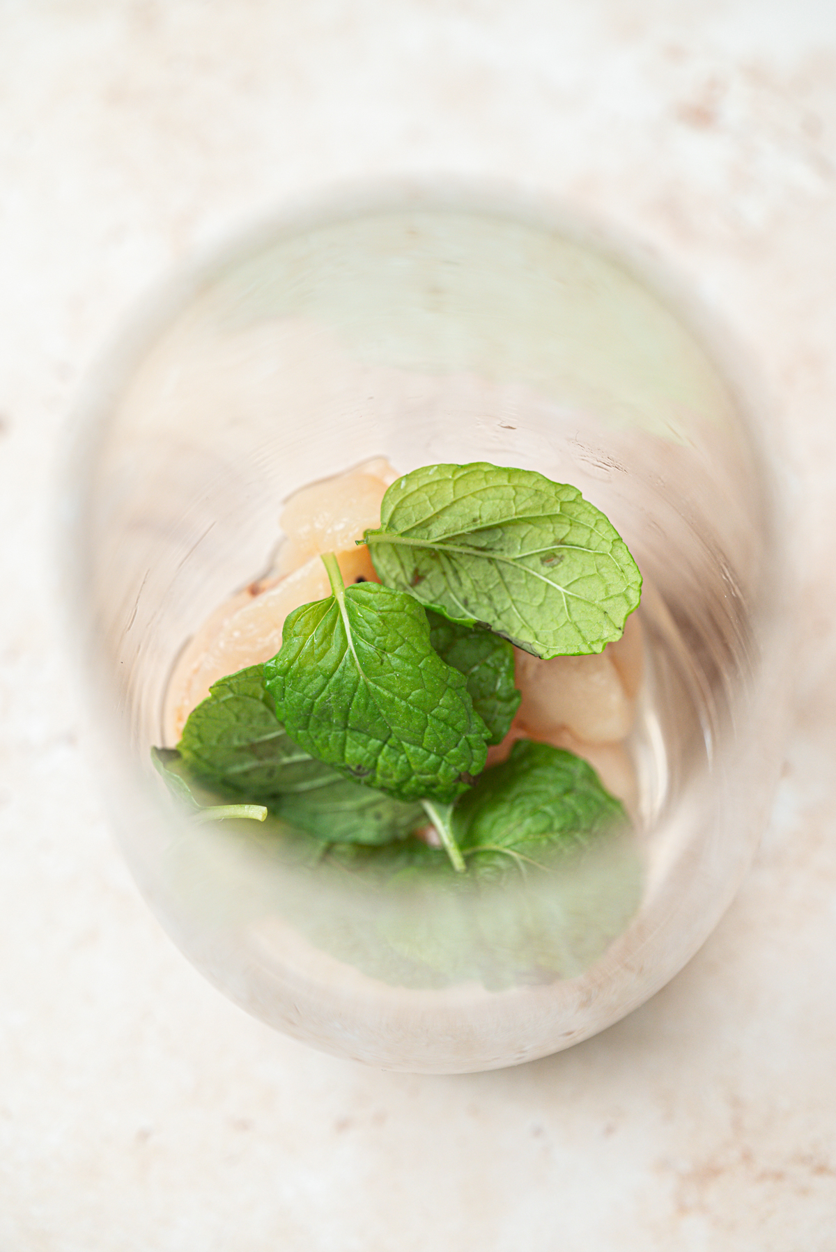 A top-down view of a glass containing ice cubes and fresh mint leaves, placed on a light-colored surface.