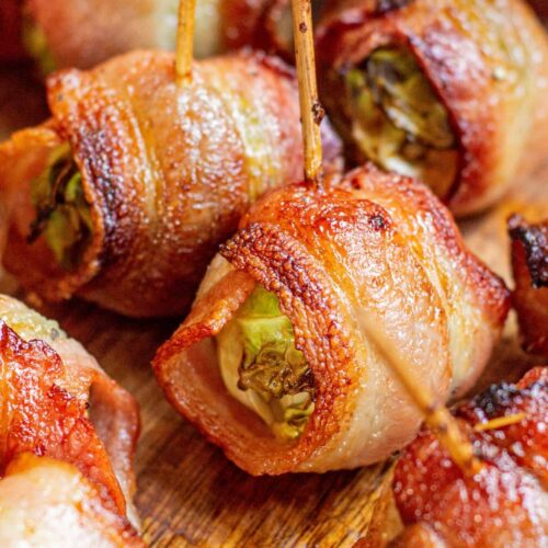 Crispy air fryer bacon-wrapped Brussels sprouts on a wooden board, each secured with a wooden toothpick, showing golden-brown, roasted edges and juicy centers.