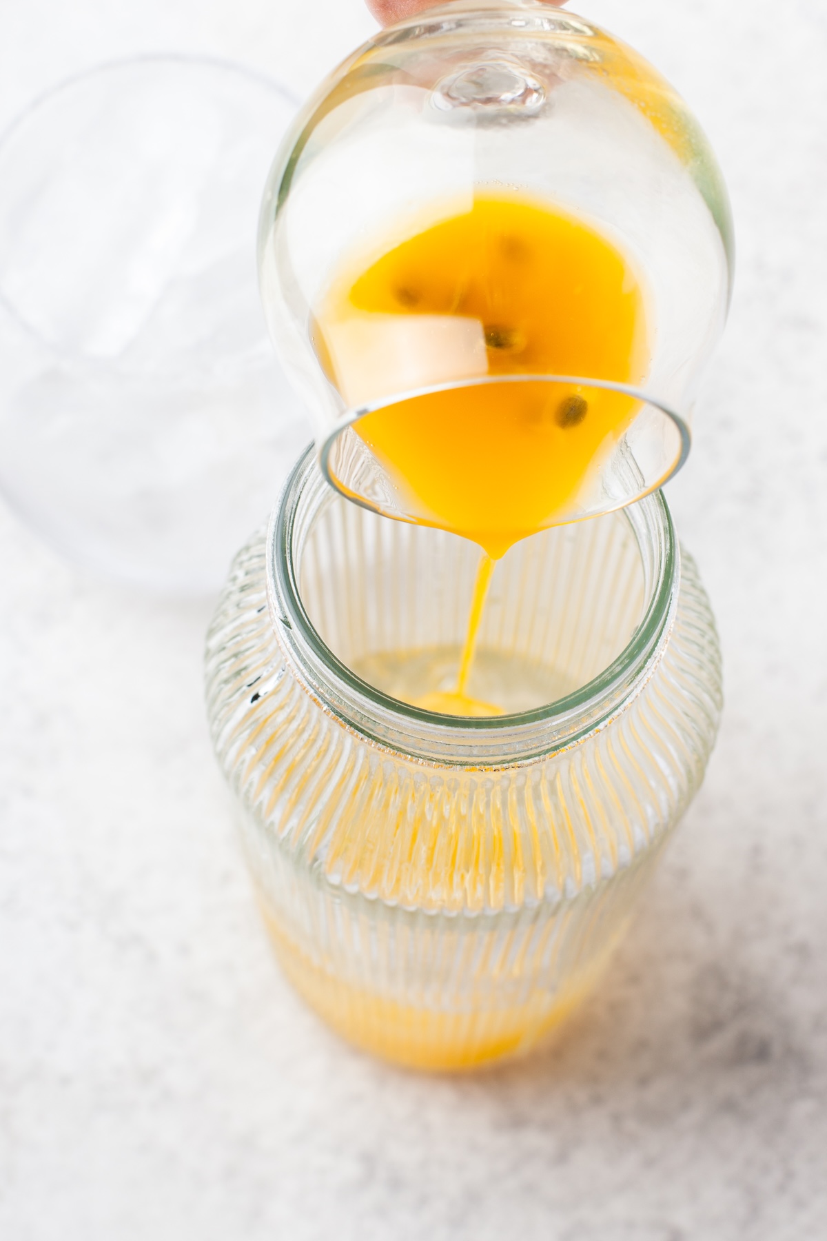 A jar is being filled with orange liquid poured through a fine mesh strainer from a glass, set on a light-colored surface.